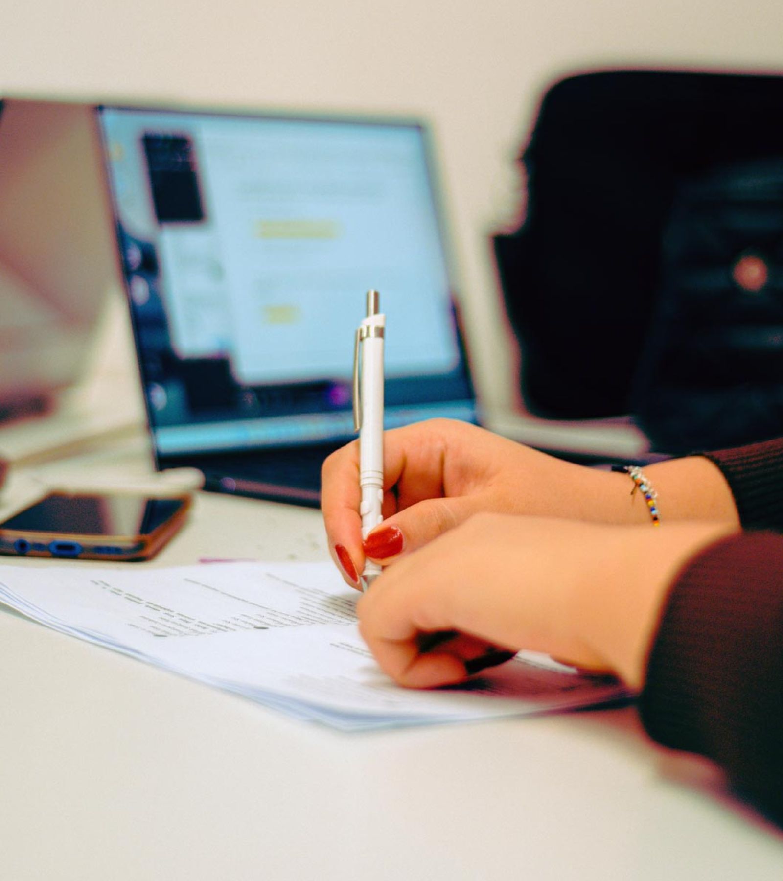 closeup of female staff member writing at desk with laptop in background